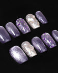 Flat lay of Amethyst Veil press-on nails with shimmering purple polish, silver glitter accents, translucent tips, and purple foil details