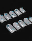 Flat lay of silver-white press-on nails with blue rhinestones and glitter tips on a black background.