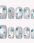 Silver and white press-on nails with blue rhinestones, glittery tips, and a soft frosted finish on a white background.