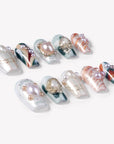 Angled flat lay of Aqua Relic press-on nails with pearls, gold shell charms, sea green accents, and orange marble patterns