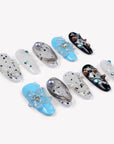 Diagonal flat lay of Artisian Orbit press-on nails with white, black, and blue accents, pearl details, and gem embellishments