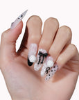 Hand model wearing Atelier Hydrangeas press-on nails with black and white floral accents, bows, and polka dots