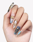 Hand model wearing Aurelia blue, pearl and gold sculpted press-on nails with metallic relief details on white