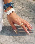 Sunlit hand wearing Aurelia turquoise, pearl and gold statement press-on nails beside layered shell bracelets