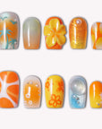 Orange and yellow press-on nails with palm tree, flower, glitter, and abstract designs on a white background.