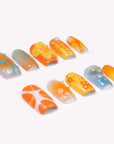 Individual press-on nail tips arranged on a white background with palm tree, flower, glitter, and abstract orange, yellow, and blue designs.