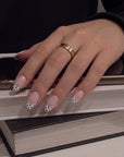 Hand model wearing Bare Polka press-on nails in nude pink with black polka dot tips while resting on books and a phone