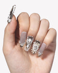 Close-up hand model wearing Baroque Crown press-on nails with silver chrome tips, white baroque scrollwork, pearls, and rhinestone crown details