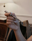 Lifestyle hand model holding a dessert fork while wearing Baroque Treasures press-on nails with pearl clusters, gold charms, and gemstone accents