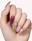Hand model wearing Berry Firelight press-on nails with burgundy tips, gold glitter accents, and gemstone details