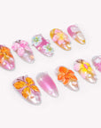 Angled flat lay of Bloom Pop pink press-on nails with raised butterflies, colorful flowers, pearls and shimmer