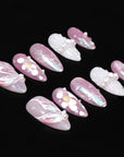 Pink and white press-on nails with pearl accents arranged on a black background.