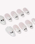 Angled flat lay of Boo Cuties press-on nails with pale pink bases, glossy white ghost tips, black eyes, and soft pink cheek dots