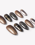 Flat lay of bronzed press-on nails with black plaid, gold stripe, and glitter accents arranged in sets