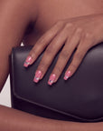 Hand model wearing Candy Spark pink press-on nails resting on a black clutch bag