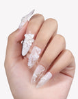 Hand model wearing Celeste white lace floral press-on nails with sculpted flowers and pearl accents on a white background