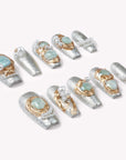 Individual Celestial Tide press-on nails arranged on a white background with silver glitter, gold swirls, pale blue stones, and pearl accents