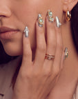 Portrait close-up of a hand model wearing Celestial Tide press-on nails with silver glitter, gold swirls, and pearl accents