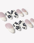 Angled flat lay of Chalk Floral press-on nails with nude pink bases, textured white French tips, and black floral accents