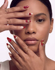 Lifestyle portrait of a hand model wearing Cherry Devotion press-on nails in red, blush, and gold with cherries, bows, and hearts