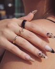 Lifestyle hand model wearing Chestnut Bloom press-on nails with nude pink bases, brown floral petals, black French tips, and gold ring styling