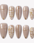 Flat lay of beige press-on nails with gold chain, gold tips, and tweed plaid accents