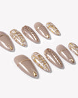 Flat lay of beige press-on nails with gold line accents, tweed plaid details, and glitter finish