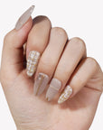 Hand model wearing beige press-on nails with gold line accents and tweed plaid details