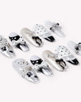 Flat lay of Coco Dot Affair press-on nails arranged in two rows with black and white polka dots, bows, lace, and pearl accents