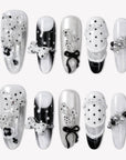 Flat lay of Coco Dot Affair press-on nails with black and white polka dots, bows, lace, and pearl accents