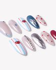 Flat lay of Cosmic Candy press-on nails with blue and white stripes, red heart charms, silver star accent, red polka dots, rhinestones, and silver cat eye design