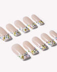 Angled flat lay of nude French tip press-on nails with multicolor rhinestones, pearls, and gold star charms on a white background