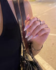 Diamond Dust pink and white glitter stiletto press-on nails shown in a street-style hand pose with silver rings