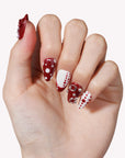Hand model wearing Dot Fantasy press-on nails in red and white with polka dots and jeweled 3D accents