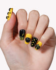 Hand model wearing Dot Obsession press-on nails in black and yellow with bold polka dots