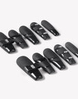 Angled flat lay of Eclipse Luxe press-on nails with black matte and glossy panel design, rectangular rhinestone accents, and sleek square tips