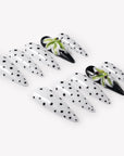 Flat lay of Eden Polka press-on nails with white bases, black polka dots, glossy black accent nails, and raised green white flower designs