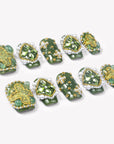 Angled flat lay of Emerald Crown press-on nails with glossy green bases, faceted green gems, pearl borders, and gold bead accents
