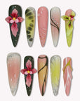 Flat lay of multicolor floral press-on nails with dark green, pink, yellow, and beige accents on a white background.