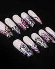 Black background flat lay of pale pink almond press-on nails with black, white, and pink butterfly accents
