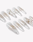 Flat lay of Frosted Ballet press-on nails with pearl white shimmer, snowflake accents, ribbon bows, and pearl embellishments