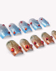 Frosted Cherry press-on nails in blue and gold glitter with red gem accents arranged in a flat lay on a white background