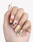 Fruit Crush cream almond press-on nails with raised peach, strawberry, lemon, cherry, and blueberry art on a hand model