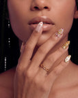 Close-up of a hand model wearing blush pink and gold jeweled press-on nails near the lips.