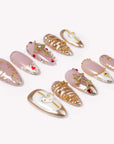 Flat lay of blush pink, white, and gold press-on nails with jeweled crosses, stars, and metallic swirl accents.