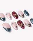 Angled flat lay of Gilded Noel press-on nails with burgundy, deep teal, nude pink, gold bow, pearls, and jewel accents