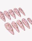 Angled flat lay of Gilded Petals press-on nails with soft pink bases and raised gold vine and petal patterns
