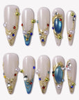 Gilded Relic Blue almond press-on nails with gold sculpted accents, pearls and colorful rhinestones in a flat lay