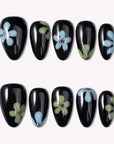 Glossy black press-on nails with blue and green flower designs arranged in two rows on a white background.