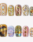Golden Muse ornate press-on nails with gold detailing, opal gems and colorful artistic designs in a flat lay